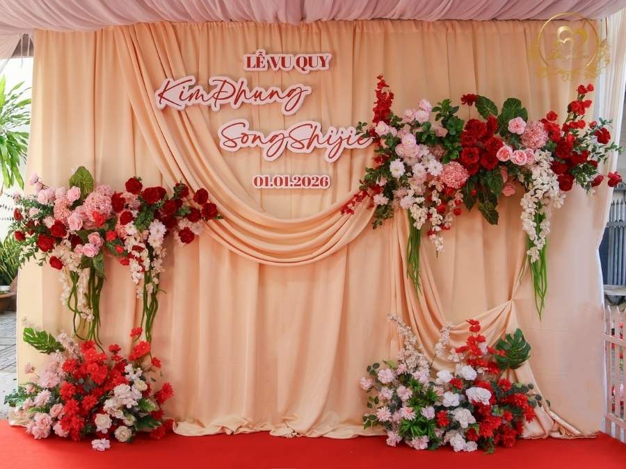 Backdrop chụp hình Lễ Vu Quy tone cam nude kết hoa đỏ nổi bật.