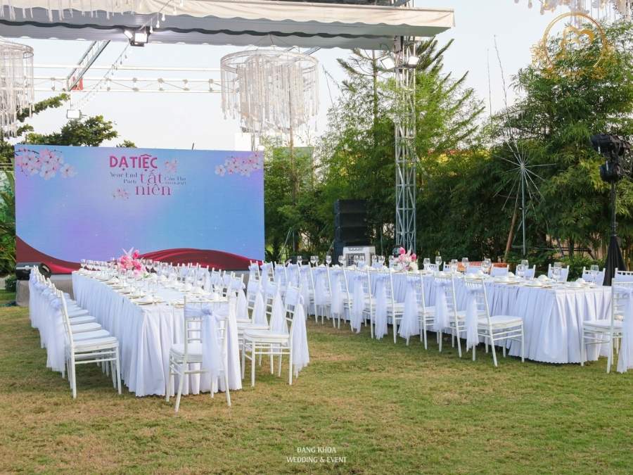Toàn cảnh không gian tiệc tất niên ngoài trời thoáng đãng với backdrop sân khấu và đèn chùm.